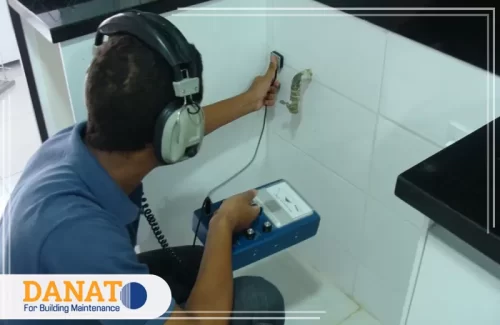 شركة اصلاح تسربات المياه في عجمان فنّيًا يستخدم جهاز كشفٍ صوتي وسماعات لتحديد موقع تسرّب خلف جدار سيراميك بدقّة ومن دون تكسير، بما يعكس خدمات شركة اصلاح تسربات المياه في عجمان المعتمدة على أجهزة حديثة وضمان إصلاح السبب الجذري.