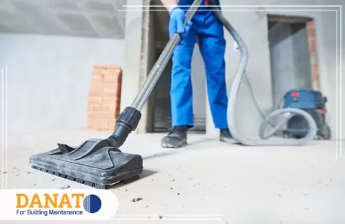 تنظيف مكيفات في العين مع تعقيم الصورة عاملًا يقوم بتنظيف المكان باستخدام مكنسة كهربائية على سطح خرساني. في هذا السياق، شركة دانات اللؤلؤ تقدم خدمات تنظيف مكيفات في العين، بالإضافة إلى تعقيم شامل للأماكن لضمان بيئة صحية ونظيفة