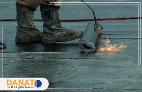 عازل مائي للاسطح في العين عاملًا يرتدي حذاءًا مطاطيًا يقوم بتركيب عازل مائي للاسطح في العين باستخدام طريقة التسخين. هذه الطريقة تعتبر من أساليب العزل الفعّالة التي تحمي الأسطح من تسرب المياه.