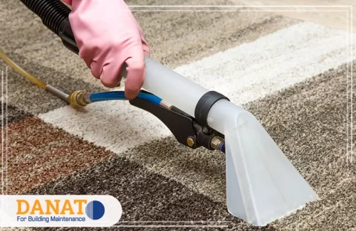 تنظيف بقع القهوة من السجاد في دبي عملية تنظيف احترافية لسجادة باستخدام جهاز شفط متطور، حيث يرتدي العامل قفازًا وردي اللون ويقوم بإزالة الأوساخ بفعالية من عمق السجاد. يبدو أن السجادة كانت متسخة ببقع داكنة، قد تكون ناتجة عن انسكاب القهوة